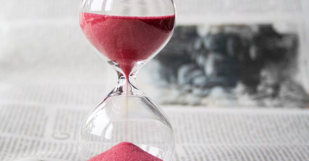 Close-up of a transparent hourglass with pink sand flowing, placed on a newspaper background.