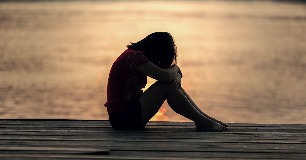 A woman sitting alone on a wooden dock by the lake, showing solitude and reflection.