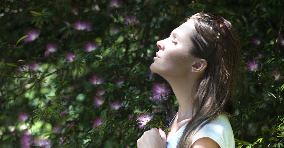 A woman enjoying a serene moment in a sunlit garden, surrounded by vibrant flowers.
