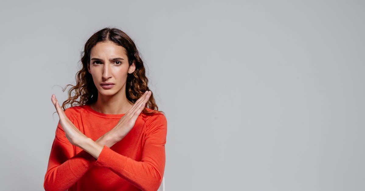 Woman with crossed arms making an X gesture against a gray background, indoor portrait.