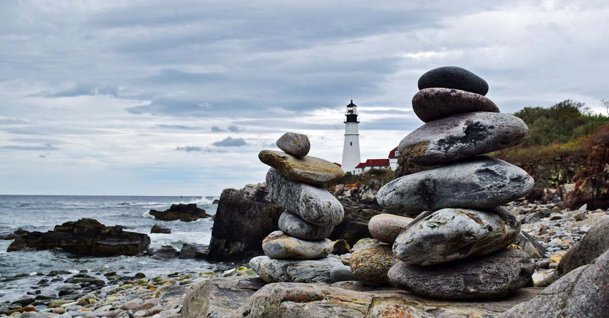 Stacked rocks by the coast with a lighthouse in the background, serene seascape.