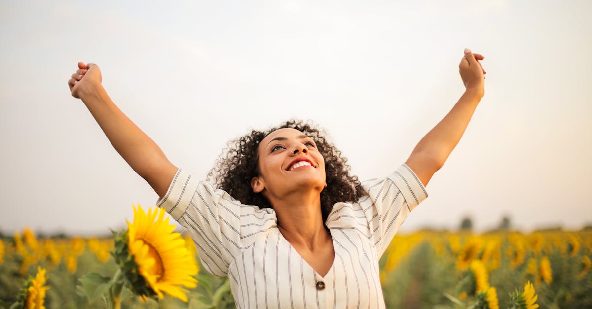 Joyful woman with arms raised in a sunflower field, embracing freedom and happiness.