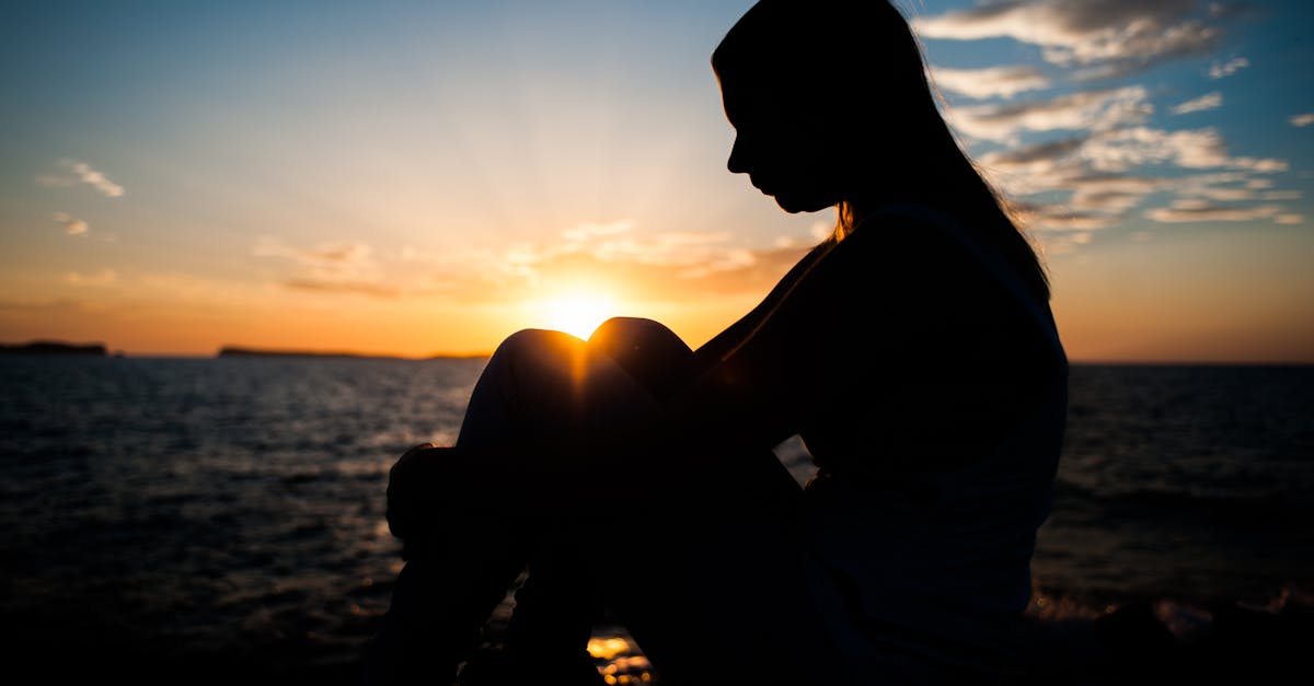 Serene silhouette of a woman seated by the sea, capturing a tranquil sunset.