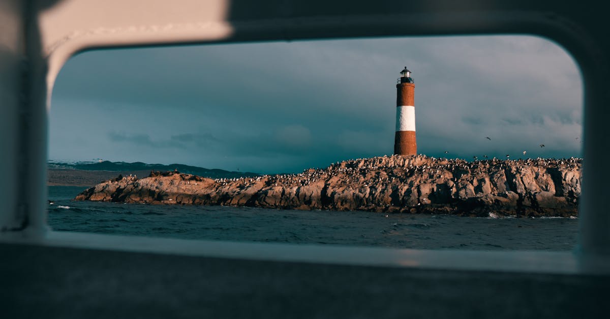 Scenic view of a lighthouse on a rocky island framed by a boat window.