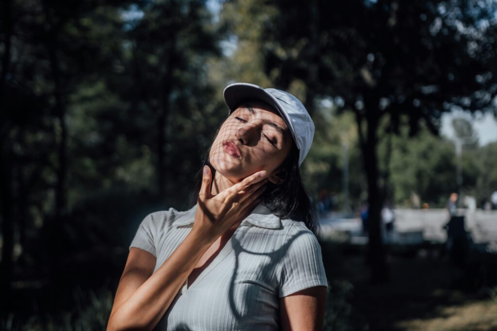 A young woman basks in sunlight with eyes closed, enjoying the tranquility of a shaded park in Mexico City.