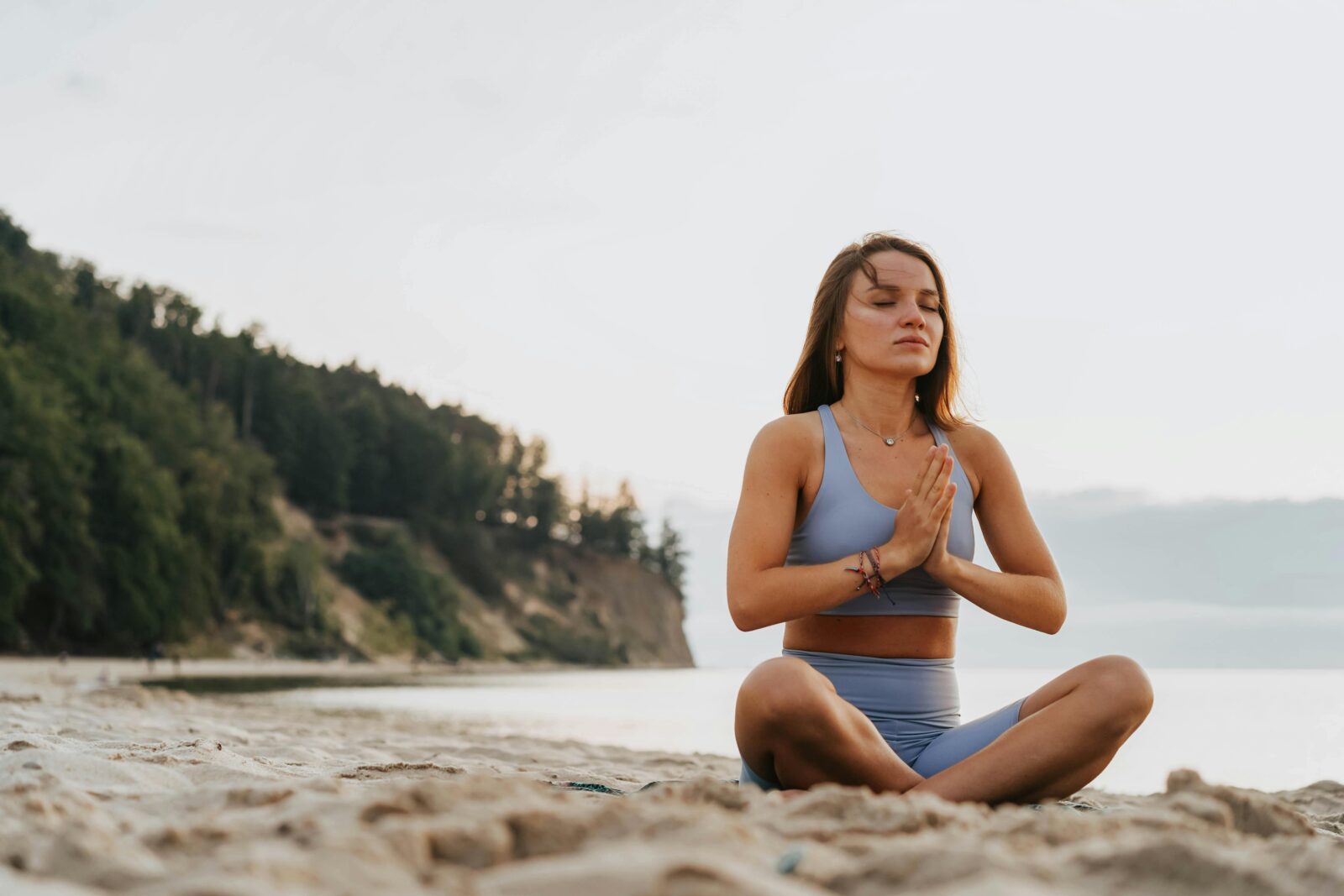 Woman practicing yoga meditation on a serene beach morning, promoting wellness.