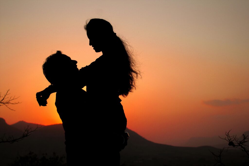 Silhouette of a couple embracing against a vibrant sunset sky.