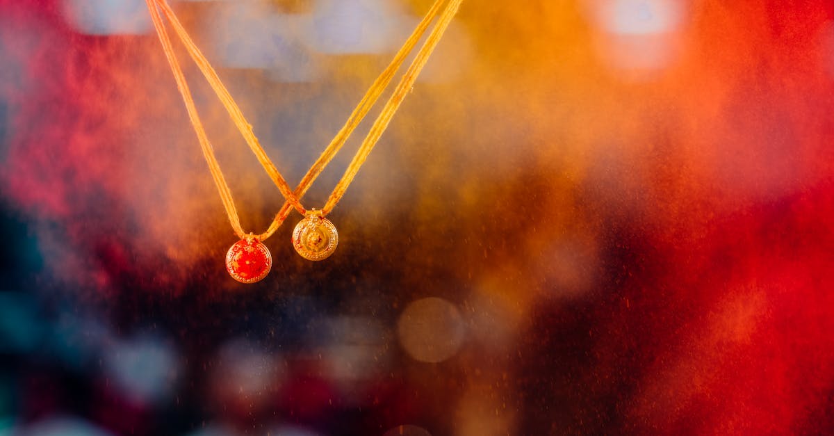 Two ornate amulets on necklaces against a vivid orange and red bokeh backdrop, symbolizing elegance.