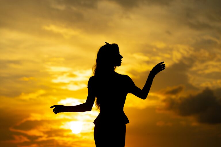 Silhouette of a woman dancing gracefully against a vibrant sunset sky.