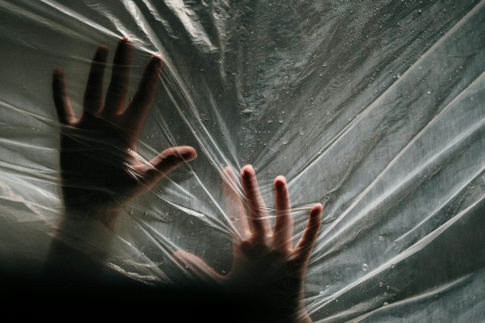 Close-up of hands pressing against a wet plastic surface, evoking a dramatic and emotional atmosphere.