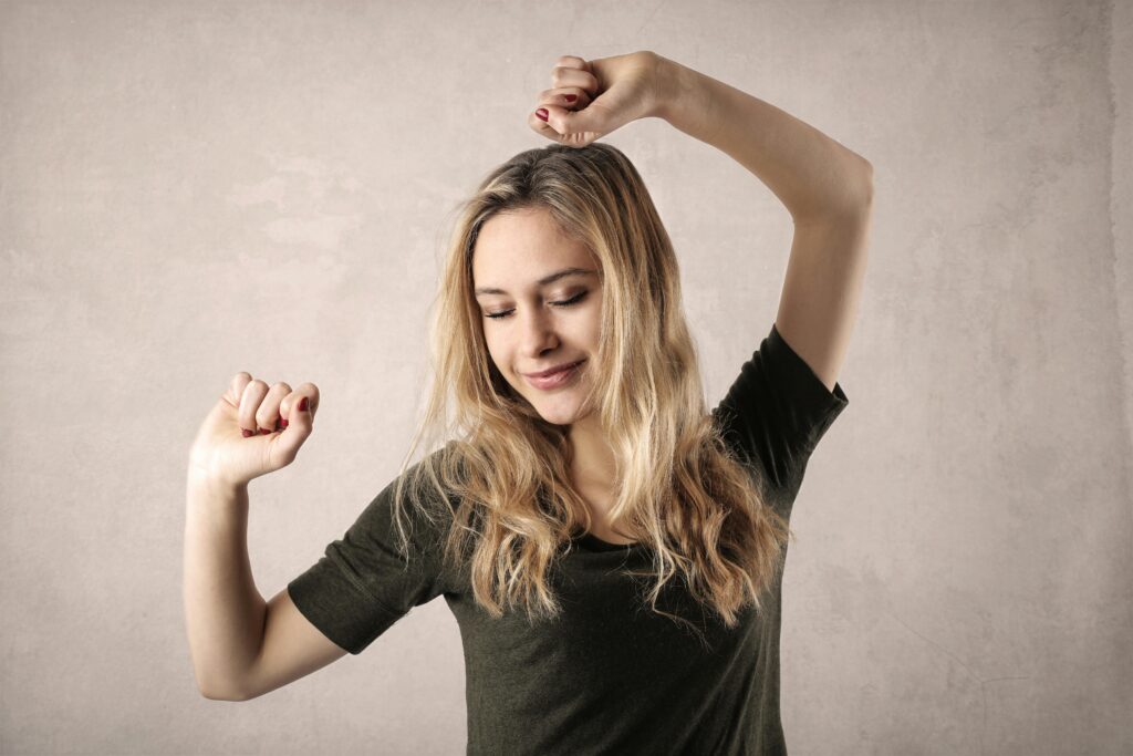 Happy young woman with blond hair dancing with joy, showcasing casual style indoors.