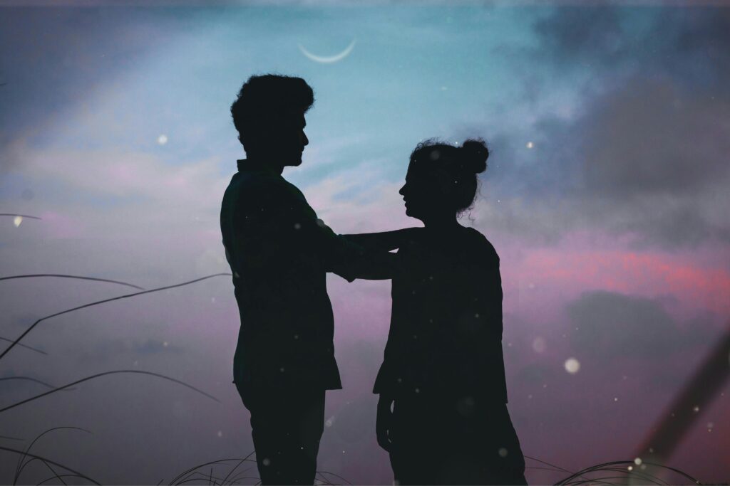 Silhouetted couple embracing under a crescent moon during twilight, creating a romantic scene.