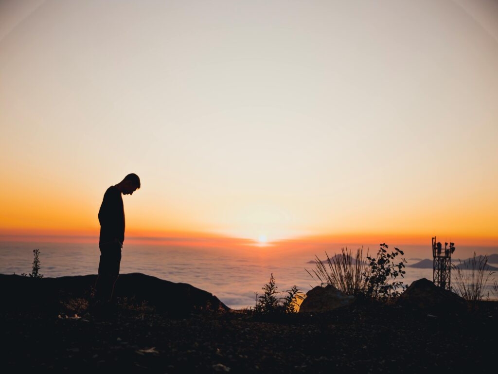 A person silhouetted against a vibrant sunset on a mountain, capturing a serene view.