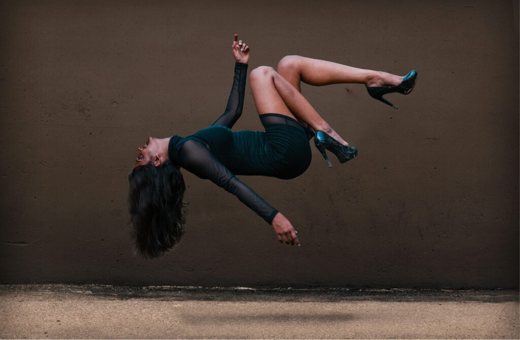 A woman in levitation pose against a textured wall, wearing an elegant dress.