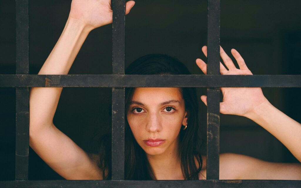 Portrait of a woman looking through iron bars, conveying emotions.