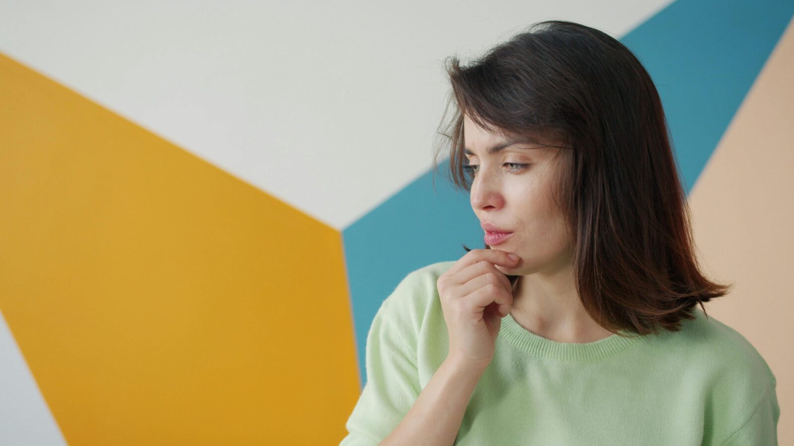 Young woman in contemplation against a colorful geometric background, indoors.