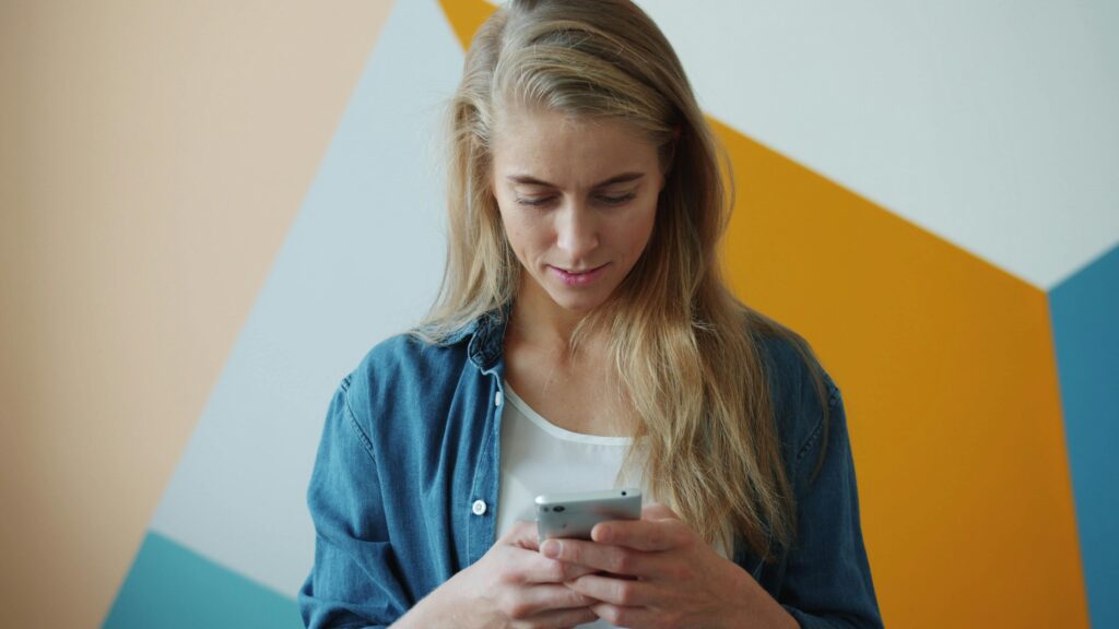 Devojka gleda u mobilni telefon ispred šarene pozadine, simbol modernih komunikacija i prepoznavanja važnih znakova u svakodnevnom životu.