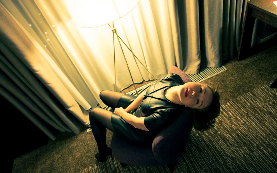 Elegant woman lounging in ambient indoor lighting, showcasing fashion in a moody setting.